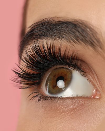 Beautiful young woman with long eyelashes on pink background, closeup